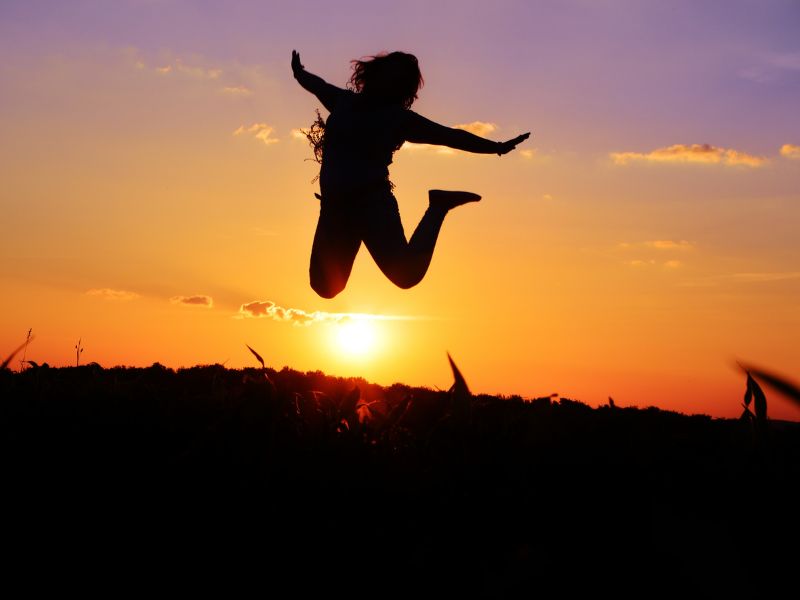 Die Silhouette einer dynamisch in die Luft springenden Person vor einem intensiv leuchtenden Sonnenuntergang als Symbol für pure Leichtigkeit.